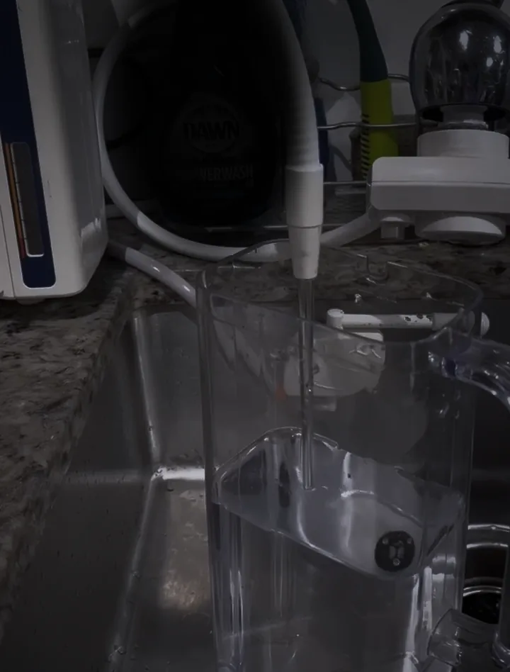 Kangen Water running from the machine's hose into a clear pitcher in the sink, in the blue light before dawn.