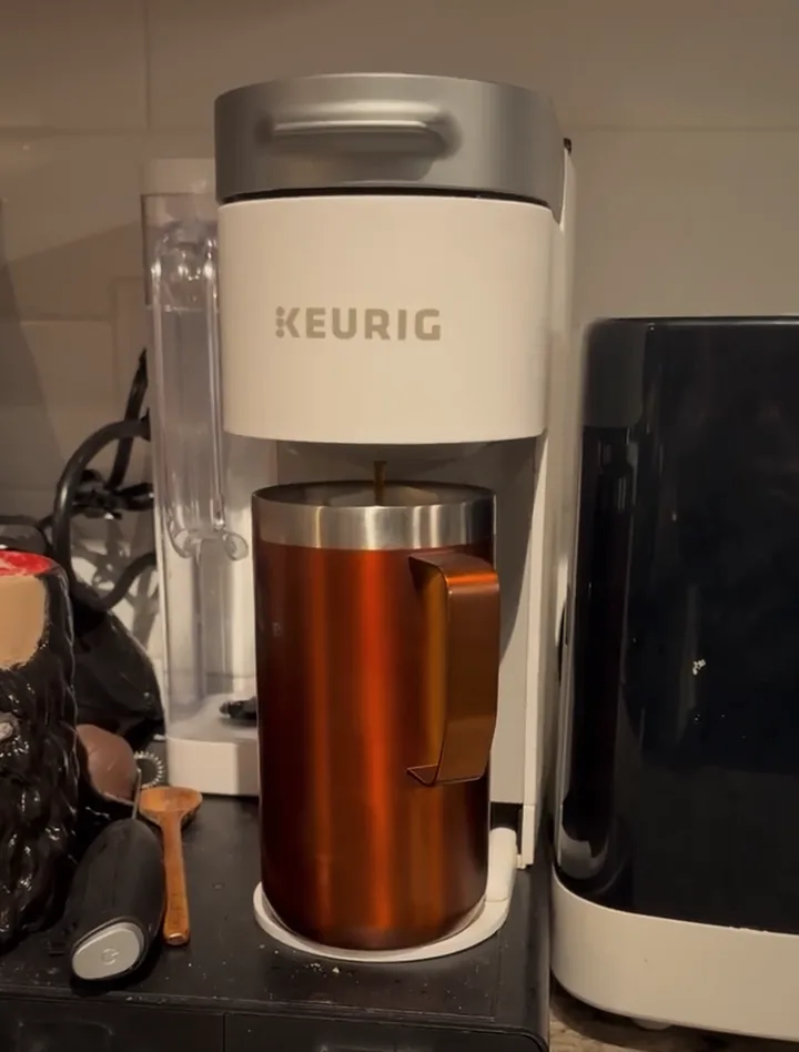 The coffee maker brewing into Face's copper mug, in warm morning light.